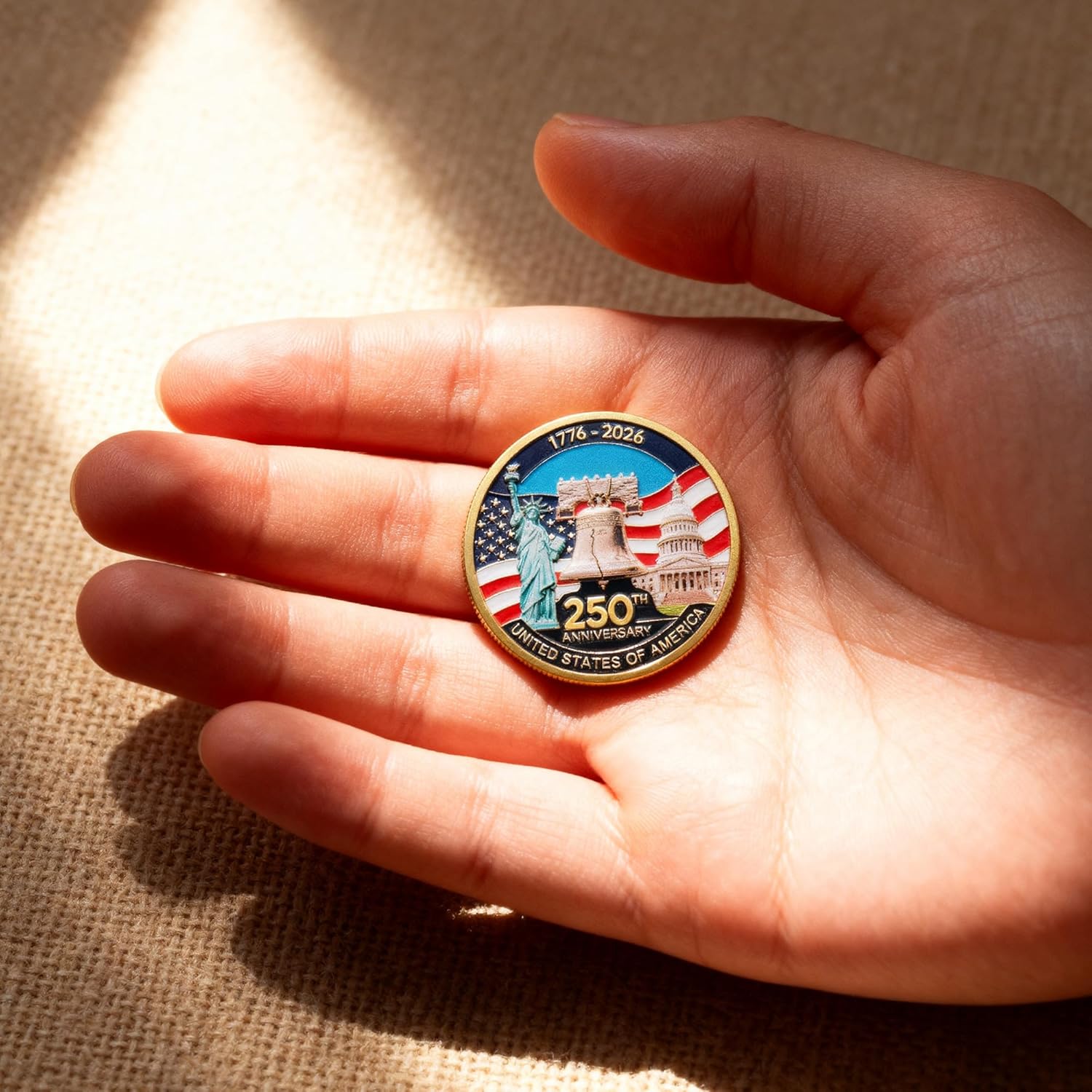 Hand holding a commemorative coin with American landmarks and '250th Anniversary' text on a textured surface.
